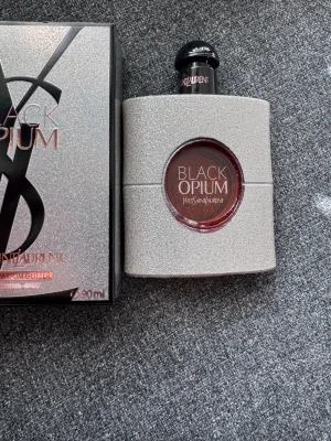 Yves Saint Laurent Black Opium Glitter - Yves Saint Laurent Black Opium Glitter är en parfym med en lyxig, glittrig silverfärgad flaska och svart kork. Doften är intensiv och modern, och flaskan har en rund öppning i mitten där parfymens namn syns. Perfekt för dig som gillar exklusiva dofter.