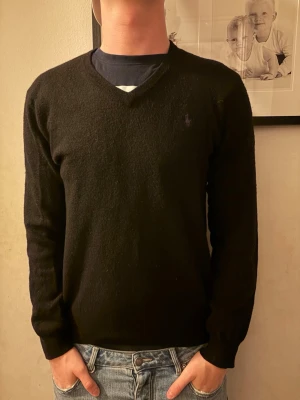 Svart kashmirtröja med v-ringning - Snygg svart tröja i mjuk kashmir med v-ringad hals. Klassisk och enkel design som passar till det mesta. Långärmad modell med normal passform och diskret broderad logga på bröstet.