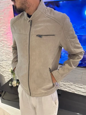 Beige skinnjacka med ståkrage - Snygg beige skinnjacka med ståkrage och dragkedja framtill. Jackan har tre fickor med dragkedja, varav en på bröstet. Stilsäker och enkel design som passar till många olika outfits.