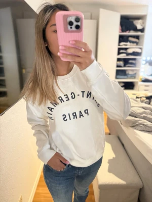 Vit sweatshirt med tryck - Vit sweatshirt med svart text 'SAINT-GERMAIN PARIS' på bröstet. Tröjan har rund halsringning och långa ärmar. Perfekt för en avslappnad och trendig stil. Storlek Xs men passa mig som bruka ha S
