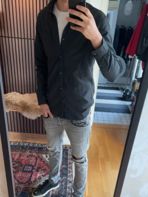 Mörkgrå skjorta med knappar - Hej, jag säljer en mörkgrå skjorta från jack&jones i storlek M. Den är i 60% bomull och 40% polyester vilket gör den lite tjockare än den flesta andra skjortorna och även skönare! Skriv vid minsta fundering eller lägg prisförslag.