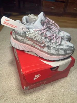 Nike silver och rosa sneakers - Jag fick den i present, men den är för liten för mig. Stolek 38. Passar 37,5 också. Nike sneakers i silver och vitt med rosa detaljer och rosa skosnören. Ovandelen är i mesh och syntetmaterial med reflekterande partier. Klassisk Nike-logga på sidan och tungan. Sitter på en vit och rosa sula med svart yttersula.