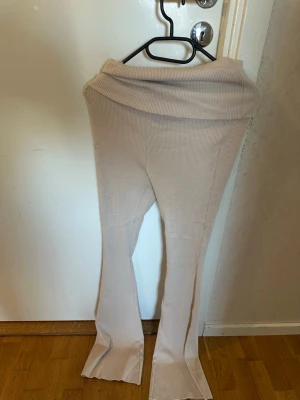 Beige ribbade leggings med slits - Säljer ett par beige leggings med ribbad struktur och utsvängda ben med slits nertill. De har en bred, vikt midja som ger en snygg och bekväm passform. Perfekta för en trendig och avslappnad look.