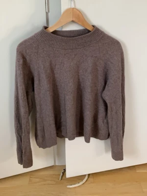 Brun stickad tröja från Wera - Mysig brun stickad tröja från Wera med rund halsringning och ribbade muddar vid ärmslut och nederkant. Tröjan har en avslappnad passform och är perfekt för lager på lager. Materialet ser ut att vara mjukt och värmande, troligen ullblandning.