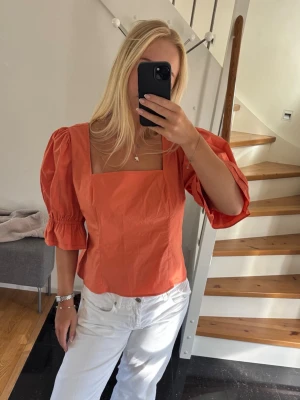 Korall topp med puffärmar och fyrkantig ringning - Trendig korall topp med fyrkantig ringning och puffiga trekvartsärmar. Toppen kan bäras både på axlarna och offshoulder för en cool look. Tillverkad i ett lätt bomullstyg som passar perfekt till sommaren.