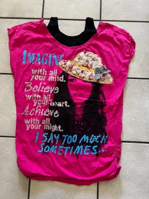 Rosa t-shirt med tryck och text storlek M/L - Cool rosa t-shirt med stort tryck av en tjej i hatt, dekorerad med blommor och rosett. Texten på framsidan är i flera färger och ger en unik look. T-shirten har korta ärmar och en avslappnad passform, perfekt för dig som gillar statement-plagg.