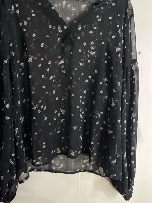 Svart blommig transparent blus -  Svart blus i transparent material med små vita blommor och v-ringning