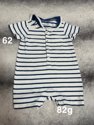 Randig babyjumpsuit med sjömanskrage - Kortärmad jumpsuit för baby i vitt med marinblå ränder, knappar framtill och liten bröstficka. Sjömansinspirerad krage bak och mjukt, bekvämt material. Perfekt för en söt och lekfull stil.🌸 Fint använt skick. Storlek 62