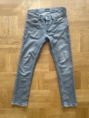 Nudie jeans - Snygga grå slim fit jeans från nudie med klassisk femficksdesign och normalhög midja. Jeansen har raka ben och råa kanter vid bensluten för en trendig look. Tillverkade i mjukt denimtyg som ger en skön känsla och bra passform.  Model grim Tim