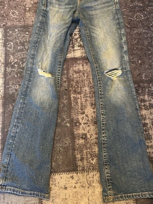 Blå bootcut jeans med slitningar - Endast upphämtning ❤️ Säljer ett par ljusblå bootcut jeans med slitningar och hål på båda knäna. Jeansen har klassisk femficksdesign och är tillverkade i denim. Perfekta för en avslappnad och trendig look.
