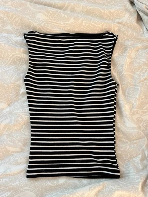 Svartvit randig ärmlös topp - Jag har aldrig använt denna och nu passar den inte. Säljer en svartvit, ärmlös topp med horisontella ränder. Toppen är figurnära och har en enkel, stilren design utan synliga detaljer.