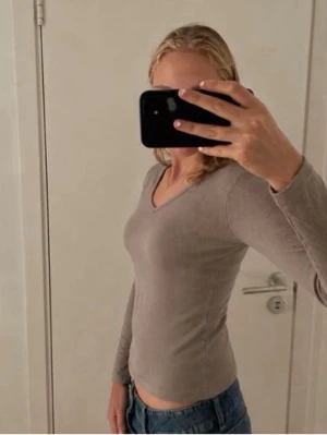 Beige långärmad v-ringad topp - Säljer en beige långärmad topp med v-ringning. Toppen har en slim passform och är tillverkad i ett mjukt material som sitter skönt mot kroppen. Perfekt att matcha med jeans eller kjol för en clean look.