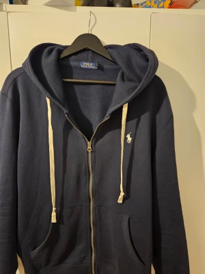 Mörkblå hoodie från Polo Ralph Lauren - Mörkblå hoodie med dragkedja från Polo Ralph Laure ENDAST använd 5 gånger känner att den sitter för dåligt på mig och vill bli av med den inget fel eller att det syns att den är använd ser helt  ny ut kom med frågor och bud ✅️
