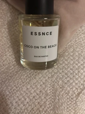 ESSNCE Coco On The Beach parfym - Fräsch Eau de Parfum från ESSNCE med namnet Coco On The Beach. Flaskan är rund och genomskinlig med svart lock och vit etikett. Innehållet är ljusgult och flaskan har en stilren, modern design som passar perfekt på parfymhyllan.