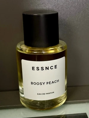 ESSNCE Boosy Peach Eau de Parfum - Boosy Peach öppnar med en söta och saftiga, men också lite bittra, persikor som följs utav noter av vita blommor. I hjärtnoterna hittar vi även rom och konjak som ger doften dess booziness och mycket karaktär. Basen består av träiga och sensuella noter, inklusive patchouli, vetiver, vanilj och kashmirträ. När doften har torkat får den en träig och pudrig sötma. Endast testad