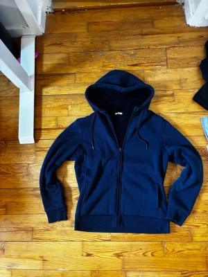 Mörkblå zip hoodie med huva ”säljer ej” - Snygg mörkblå hoodie med dragkedja framtill och justerbar huva. Tröjan har långa ärmar, ribbade muddar och två fickor på sidorna. Perfekt för chill dagar eller när du vill ha en enkel och stilren look. säljer inte just nu