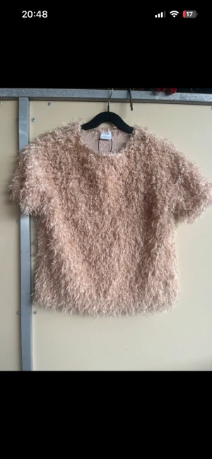 Beige fluffig topp med kort ärm - Supermjuk och fluffig beige topp från Monki med korta ärmar och rund hals. Den har en cool textur som ger en unik look och är perfekt för dig som vill sticka ut lite extra. Passar lika bra till jeans som till kjol. Passar 152-158