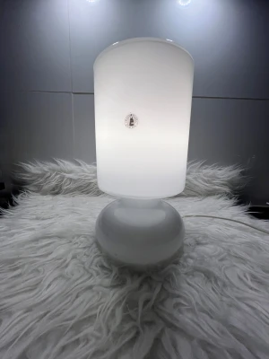 Ikea lykta  - Bilderna visar en vit bordslampa i glas med rund fot och cylinderformad skärm. Lampan har en modern och stilren design, och ser ut att vara i mycket gott skick utan synligt slitage eller defekter. Perfekt som dekorativ belysning i hemmet.