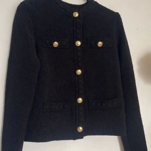 Svart kofta med guldknappar från H&M XS - Svart cardigan jacka från H&M i stickat material med snygga guldknappar framtill och på fickorna. Jackan har rund hals, långa ärmar och två dekorativa bröstfickor. Perfekt för dig som gillar klassisk och chic stil.