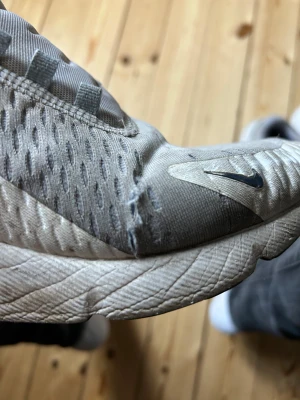 Nike Air Max 270 vita och röda sneakers - Nike Air Max 270 sneakers i vitt med röda och marinblå detaljer. Skorna har en synlig röd Air Max-sula, mesh-överdel med ventilerande hål och snörning. Swoosh-logga i rött och svart på sidan och fram. Snygg sportig look med platt sula och rund tå.