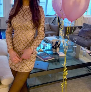 Champagnefärgad klänning med guldmönster - Säljer en champagnefärgad klänning med glittrigt mönster i guld. Klänningen har en figurnära passform och är perfekt för dig som vill sticka ut med en elegant och trendig look. 