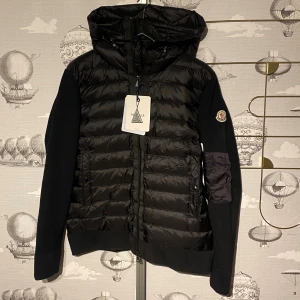 Svart pufferjacka från Moncler - Svart pufferjacka från Moncler med huva och dragkedja framtill. Jackan har quiltad front i glansig syntet och stickade ärmar med Moncler-logga på vänster arm. Snygg, modern look med praktiska fickor och ribbade muddar. Super fin kvalité, Perfekt för kallare tider. Tveka inte på att skriva om du har frågor eller funderingar. Mvh Rs1an✌️