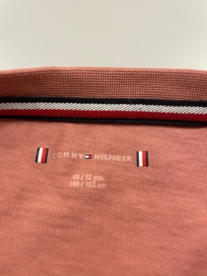 Rosa t-shirt från Tommy Hilfiger - Snygg rosa t-shirt från Tommy Hilfiger med klassisk logga broderad på bröstet. T-shirten har rund hals och korta ärmar, tillverkad i bomull.