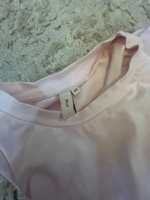Ljusrosa t-shirt från Nelly XS - Säljer en ljusrosa t-shirt från Nelly i storlek XS. T-shirten har en loose passform och är tillverkad i mjuk bomull. Den är enkel och stilren utan mönster eller detaljer, med klassisk rund hals och korta ärmar. Perfekt för dig som gillar basic och comfy vibes.