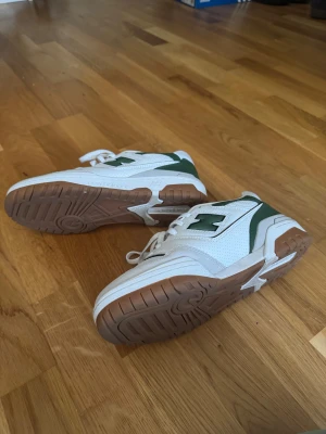 New Balance 550 vita och gröna sneakers - Säljer ett par New Balance 550 sneakers i vitt och grönt med bruna gummisulor. Skornar har endast provats på och är oanvända. Nypris ca 1700 kr (kolla på andra modeller på new balances webbsida). 