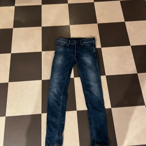 Blå skinny jeans från Diesel, storlek 29 - Snygga blå jeans från Diesel i skinny fit med klassisk femficksdesign och diskret slitning. Jeansen är tillverkade i stretchigt denimmaterial med 95% bomull och 2% elastan för skön passform. Perfekta för dig som gillar en smal siluett och stilren look.