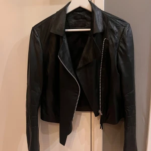 Svart skinnjacka Tiger of Sweden - Svart skinnjacka från Tiger of Sweden Jeans i croppad modell med asymmetrisk dragkedja och klassisk krage. Jackan har långa ärmar med snygga detaljer och dragkedjor vid ärmsluten. Perfekt för dig som vill ha enstilren look. Fint tunnt och mjuk skinn. Jackan är använd vi ett fåtal tillfällen. Passar lien m och s. Nypris 6000kr
