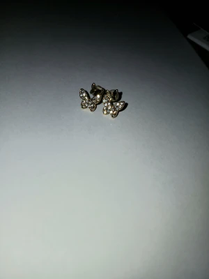 Glittriga fjärilsörhängen i guld. - Supersöta örhängen i form av fjärilar med gnistrande stenar. De är i guldfärg och har små vita stenar som ger en glittrig effekt. Perfekta för dig som vill ha något gulligt och trendigt i öronen.❤️