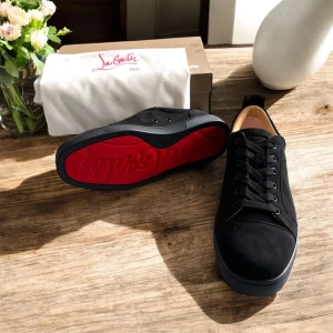 Svarta sneakers från Christian Louboutin - Snygga svarta sneakers från Christian Louboutin med ikonisk röd sula och rund tå. Skorna har snörning, platt sula och är tillverkade i mocka med mjukt skinnfoder. Perfekt för dig som vill ha en stilren och lyxig look med en touch av attityd.