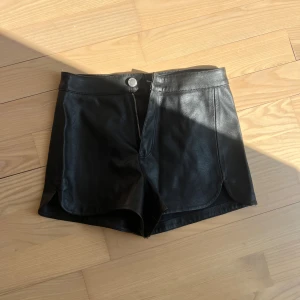 Svarta skinnshorts från H&M Divided - Snygga svarta shorts i skinnimitation från H&M Divided. De har en klassisk midja, dragkedja framtill och knappstängning. 
