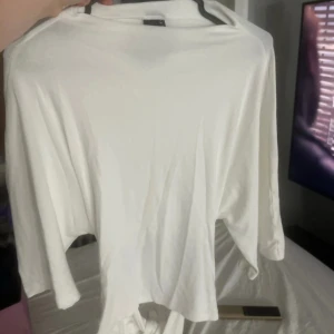 Vit långärmad topp från Gina Tricot - Säljer en vit långärmad topp från Gina Tricot i mjuk bomull. Toppen har en enkel och clean design med rund hals och knytning framtill som ger en snygg detalj. Perfekt att styla med jeans eller kjol för en chill look. Aldeig använd men prislappen är av 