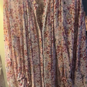 Blommig blus  By Malina XL - Superfin blus från By Malina i storlek XL. Blusen har ett romantiskt blommigt mönster i rosa, lila och beige toner, med långa ärmar och knappar framtill. Tillverkad i ett mjukt, flowy material som känns lyxigt och luftigt.