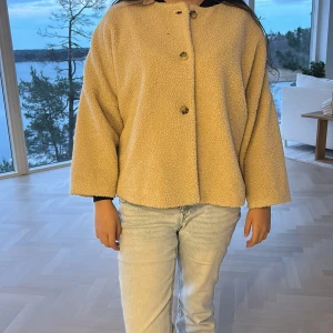 Beige teddyjacka med knappar från Sandro - Säljer en beige teddyjacka från Sandro med rak och loose passform. Jackan har tre knappar framtill och är tillverkad i mjukt fleece-material. Den har långärmade, vida ärmar och en enkel, stilren design som är perfekt för att hålla sig varm och se chill ut. 🤎🤎 skriv gärna vid funderingar och intresse! 🌟💫