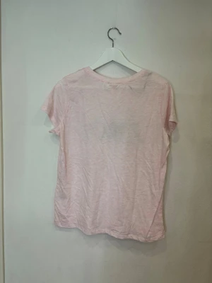 Rosa t-shirt med Disney-tryck från H&M - Söt ljusrosa t-shirt från H&M med svart 'love'-tryck där O:et är en siluett av Musse Pigg. T-shirten har rund hals, korta ärmar och är gjord i mjuk bomull. Perfekt för dig som gillar Disney och vill ha en chill look.