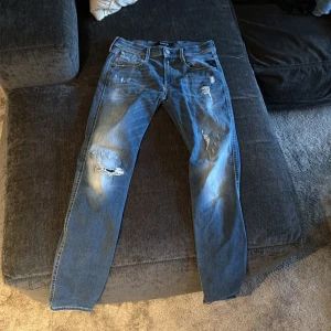 Replay jeans med slitningar, blå, W28 L32 - Snygga blå jeans från Replay med coola slitningar och distressed detaljer på benen. Klassisk femficksmodell med normal passform och raka ben. Jeansen har låg midja och är tillverkade i mjukt bomullsmaterial för skön känsla. Perfekt för dig som gillar en avslappnad streetstil.