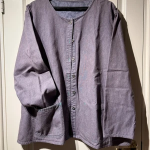 Grå overshirt och matchande byxor från Gudrun Sjödén - Overshirt i grå bomull från Gudrun Sjödén med avslappnad passform, rund halsringning och knappar framtill. Skjortan har en stor ficka på ena sidan och synliga sömmar i kontrasterande färg. Säljes med matchade byxor! 