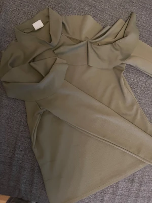 Olive ärmlös tröja Gina Tricot - Snygg beige klänning från Gina Tricot i storlek L. Modellen är ärmlös med en cool krage och omlott-detalj framtill. Materialet känns mjukt och har en lätt struktur, perfekt för dig som gillar stilrena och moderna plagg.