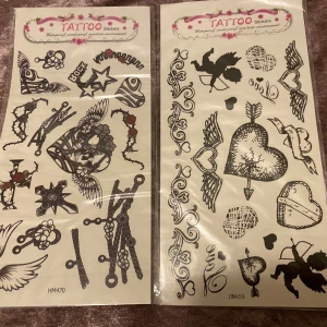 Tattoo stickers med hjärtan och vingar - Två ark med tattoo stickers i svart och rött, med motiv som hjärtan, vingar, stjärnor, amor, rosor och kedjor. Perfekt för att skapa en edgy look med tillfälliga tatueringar. Motiven är detaljerade och varierar mellan romantiska och rockiga stilar.