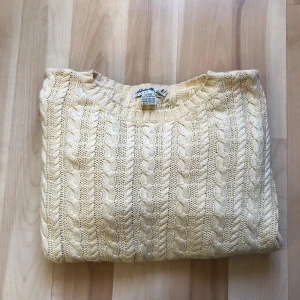 Beige kabelstickad tröja Eddie Bauer - Kabelstickad tröja från Eddie Bauer i storlek L. Färgen är beige och materialet är 100% bomull. Tröjan har rund hals och långärmade ärmar, med klassiskt flätmönster som ger en chill och tidlös vibe.