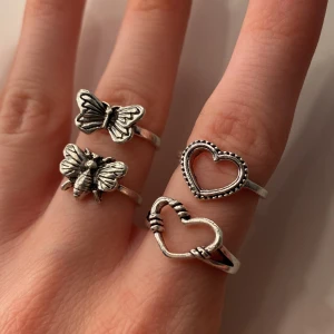  silverfärgade ringar fjäril & hjärta - Fyra snygga silverfärgade ringar i olika designer: en med fjäril, en med bi, och två med hjärtformade detaljer. Dessa är helt oanvända och är ej av äkta silver. Alla för 15kr! ❤️