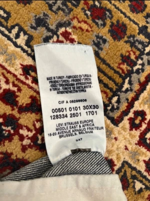 Levi's 501 blå jeans W30 L30 - Klassiska Levi's 501 jeans i mörkblå tvätt med raka ben och knappgylf. Jeansen har fem fickor, kontrastsömmar och den ikoniska läderpatchen bak i midjan. Perfekt för dig som gillar tidlös stil och äkta denim.