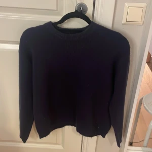 Mörkblå stickad tröja 157 - Mörkblå stickad tröja från 157 med rund hals och långa ärmar. Tröjan har en enkel och klassisk design med ribbad kant vid halsen och nederdelen. Perfekt för dig som gillar basic och vill ha något mjukt och skönt till hösten eller vintern.