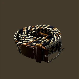 Randigt flätat bälte med skinn - Snyggt flätat bälte med randigt mönster i marinblått, beige och brunt. Spännet är i silverfärgad metall och ändarna är förstärkta med brunt skinn. Perfekt för att ge outfiten en cool och stilren touch.