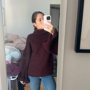 Vinröd polotröja med öppen rygg och vida ärmar - Säljer en vinröd stickad polotröja med krage och snygga vida ärmar. Tröjan är öppen i rygg och har en omlott-detalj  som ger en cool och unik look. Perfekt att styla med jeans eller kjol för en trendig vibe.