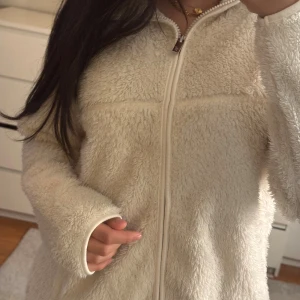 Vit teddyjacka med dragkedja - Mysig vit teddyjacka med fluffigt material och hel dragkedja framtill. Jackan har långärmade ärmar. 