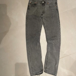 Levis 501 grå jeans straight fit - Grå Levis 501 jeans med klassisk straight fit och hög midja. Jeansen har fem fickor, knappgylf och den ikoniska Levis-lappen bak. Tillverkade i slitstark denim med rå kant vid benslut för en cool vibe.